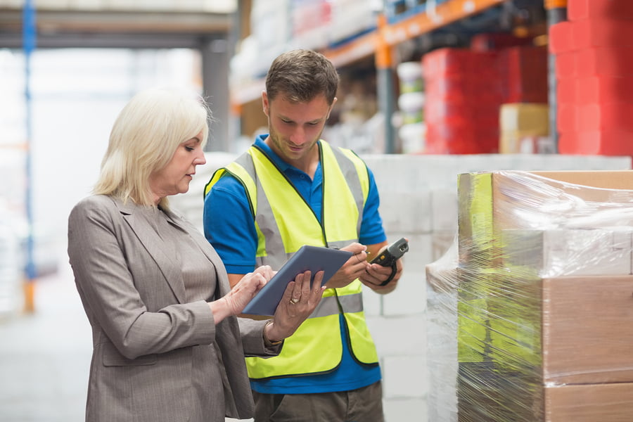 Manager using tablet while worker scanning package in warehouse